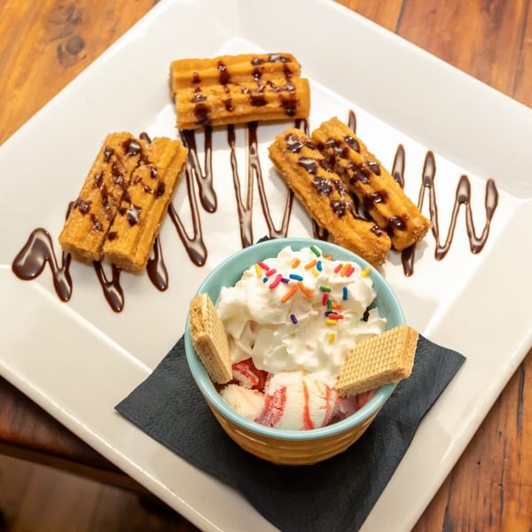 Tostao's churros with chocolate drizzle and a bowl of ice cream with whipped cream and sprinkles.