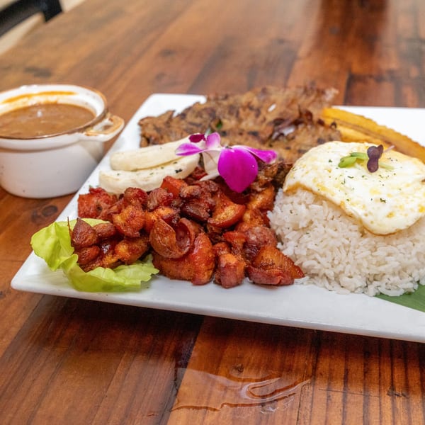 A Tostao's Tapas-bar platter with fried pork, rice, fried egg, plantains, and a side of sauce.