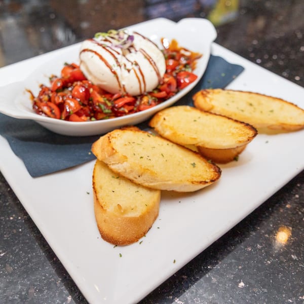 Burrata cheese with balsamic glaze and cherry tomatoes, served with toasted bread on a white plate.