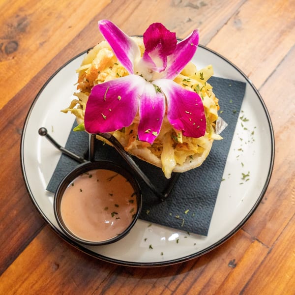 Tostao's tapas dish with shredded chicken, cabbage, and a pink orchid, served with sauce.