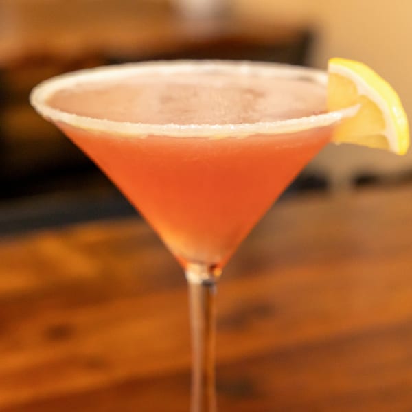A vibrant red cocktail in a martini glass, garnished with a lemon slice and sugar rim.